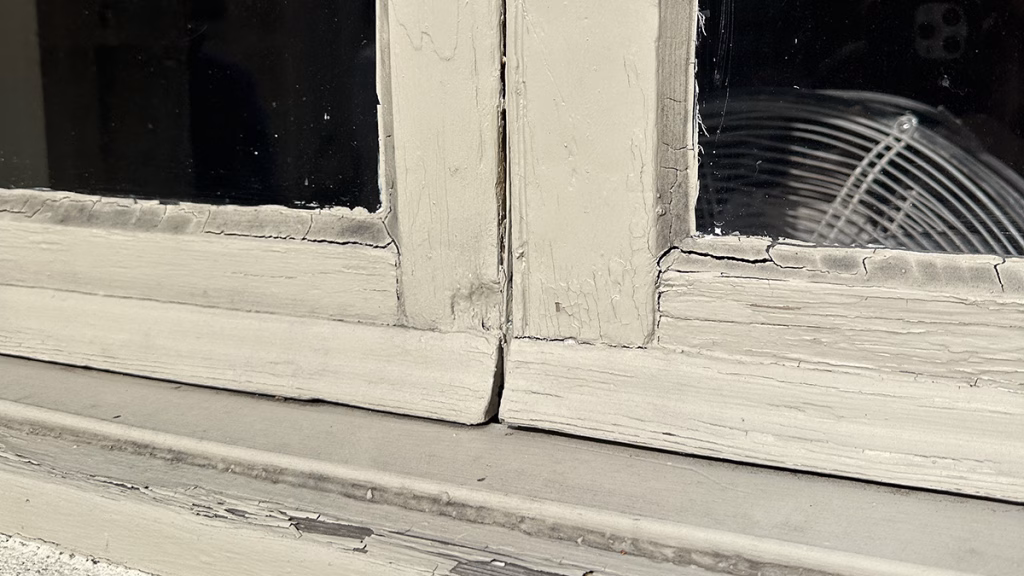 Close-up of historic window restoration showing cracked glass and worn wood frame.